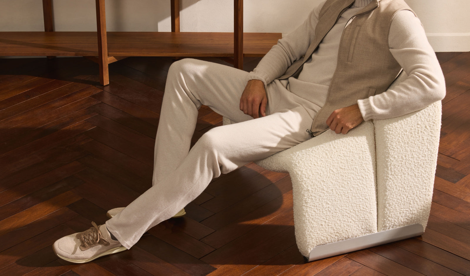 Model seated wearing a cream knit, linen gilet and tailored trousers