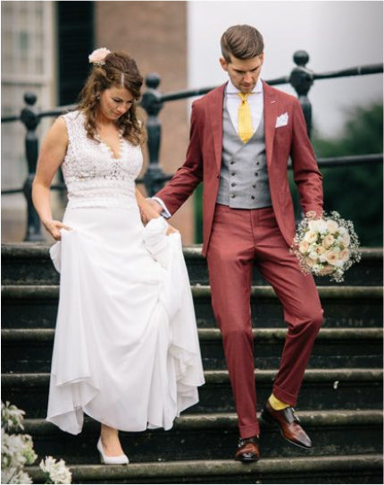 Harald and his bride on the steps on their wedding day, he in a red suit with a grey waistcoat